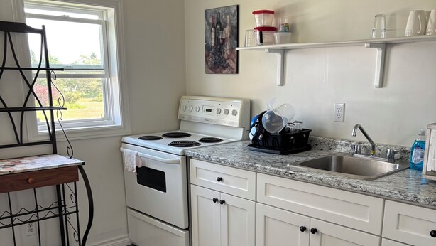 A kitchen with white cabinets, a stove, a sink, and a window.