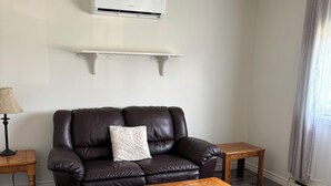 A living room with a leather sofa, a wooden coffee table, a lamp, and an air conditioning unit on the wall.