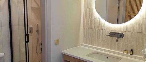 A modern bathroom with a glass shower enclosure, a wooden vanity with a sink, and a large mirror with a textured backsplash.