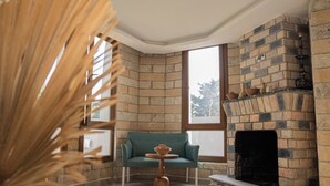 Ein Eckzimmer mit Kamin aus Ziegelsteinen, einem türkisfarbenen Sofa und einem kleinen runden Tisch.