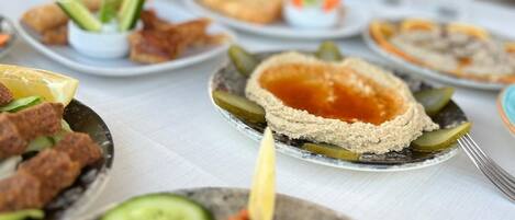 Une table dressée avec divers plats, notamment du houmous, des cornichons et une sauce rouge, ce qui laisse supposer qu’il s’agit d’un repas.
