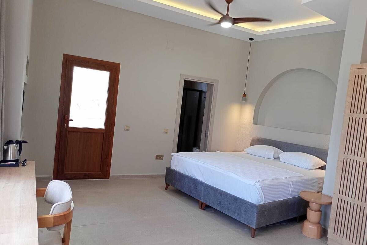 Een slaapkamer met een bed, een plafondventilator, een deur en een klein tafeltje.