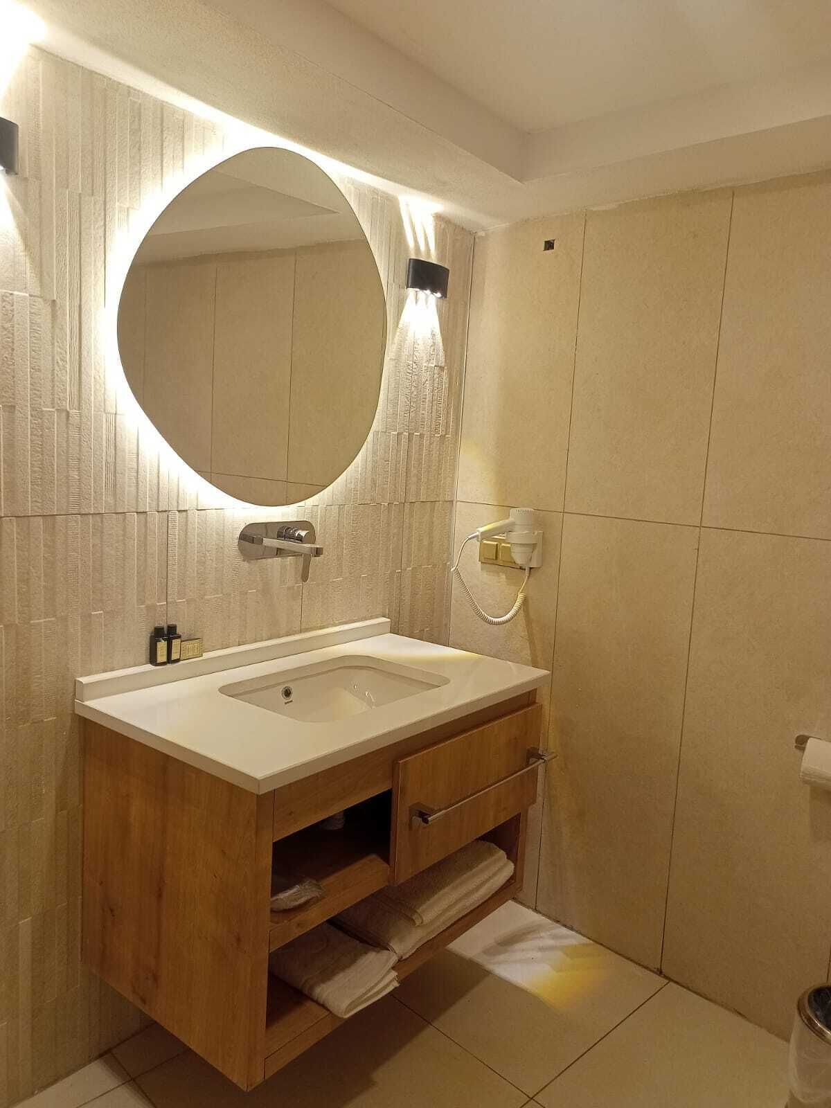 A modern bathroom with a wooden vanity, a large mirror, and a built-in towel rack.