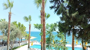 Ein Poolbereich eines Resorts mit Palmen, blauem Himmel und Blick auf das Meer.