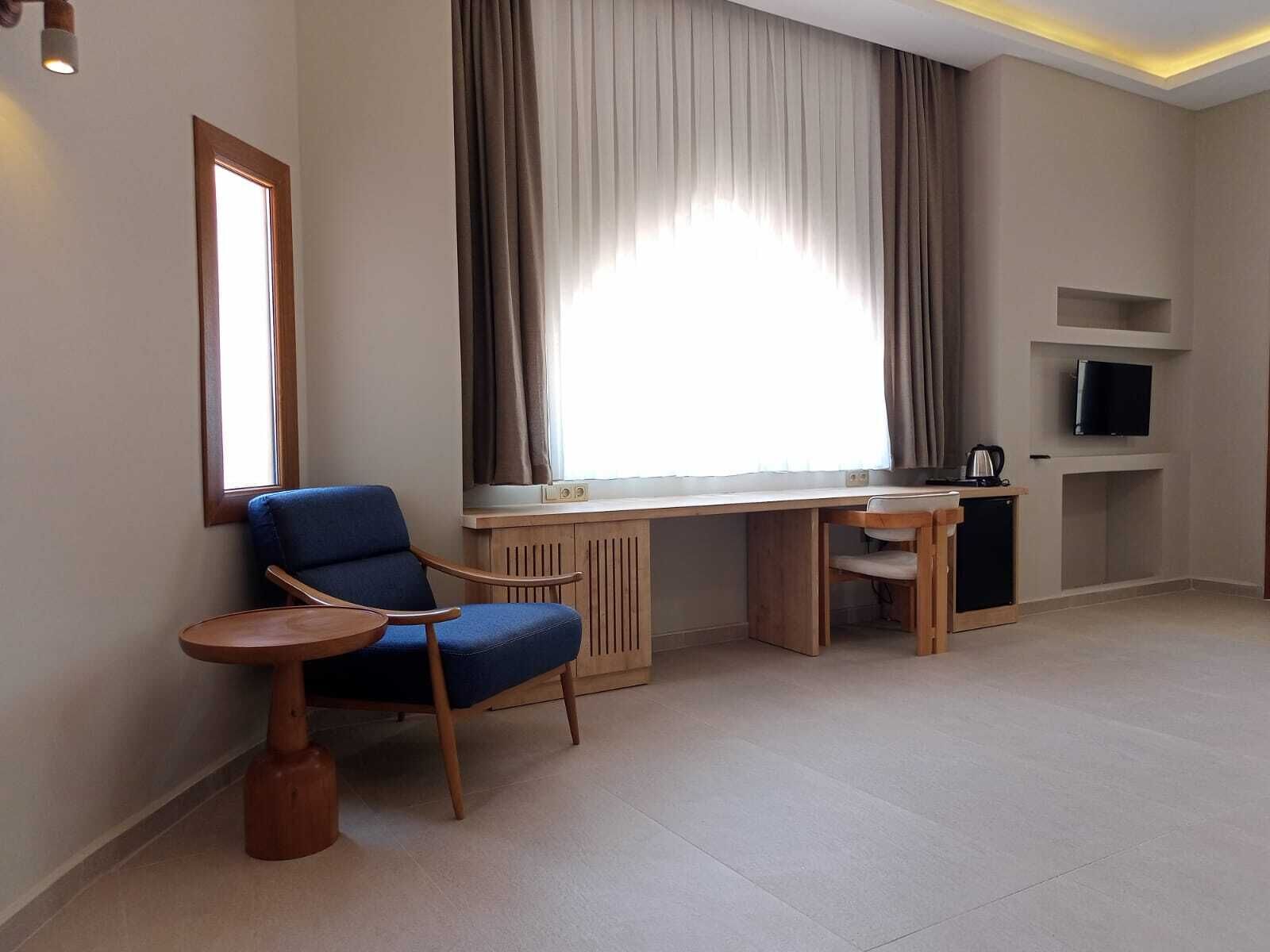 Una sala de estar moderna con un sillón azul, un escritorio de madera, una mesita pequeña y un televisor sobre una estantería.