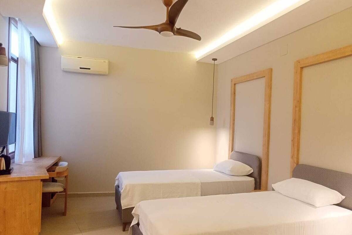 Een hotelkamer met twee bedden, een bureau, een stoel, een plafondventilator en een airconditioning.