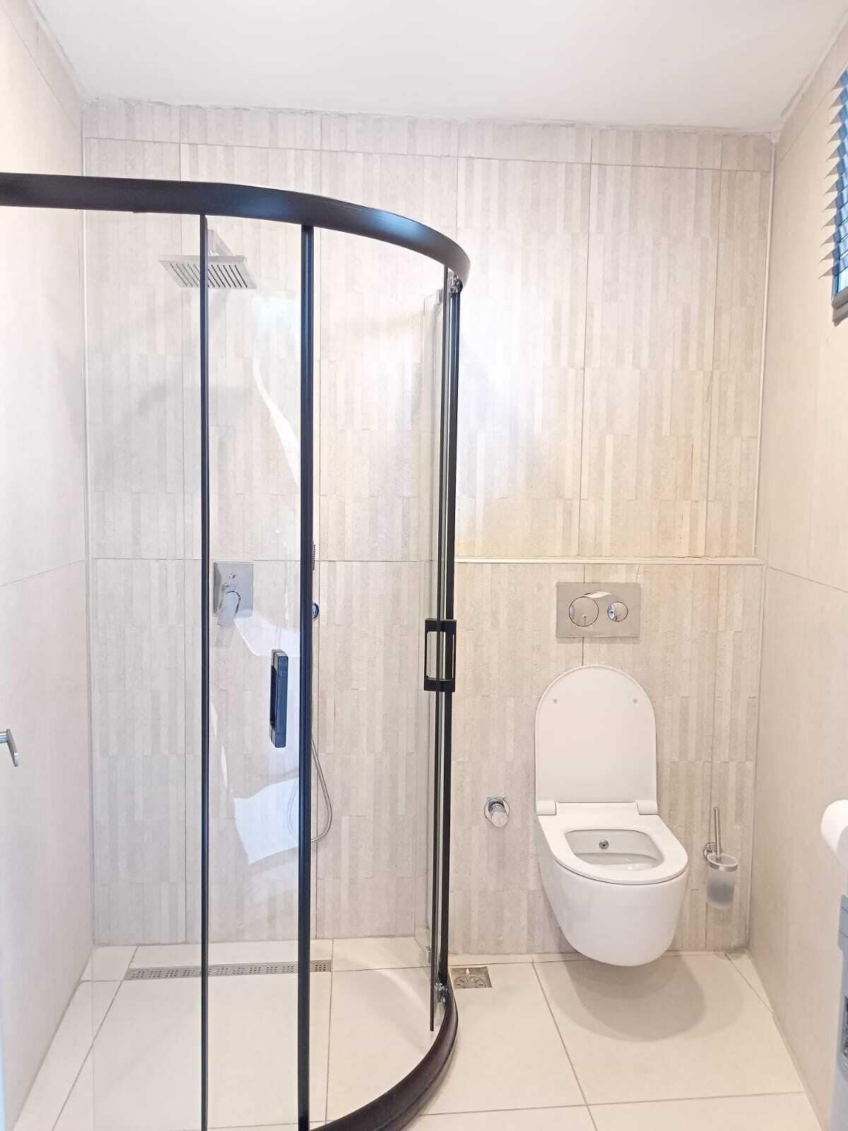 Uma casa de banho moderna com chuveiro de vidro, sanita e lavatório.