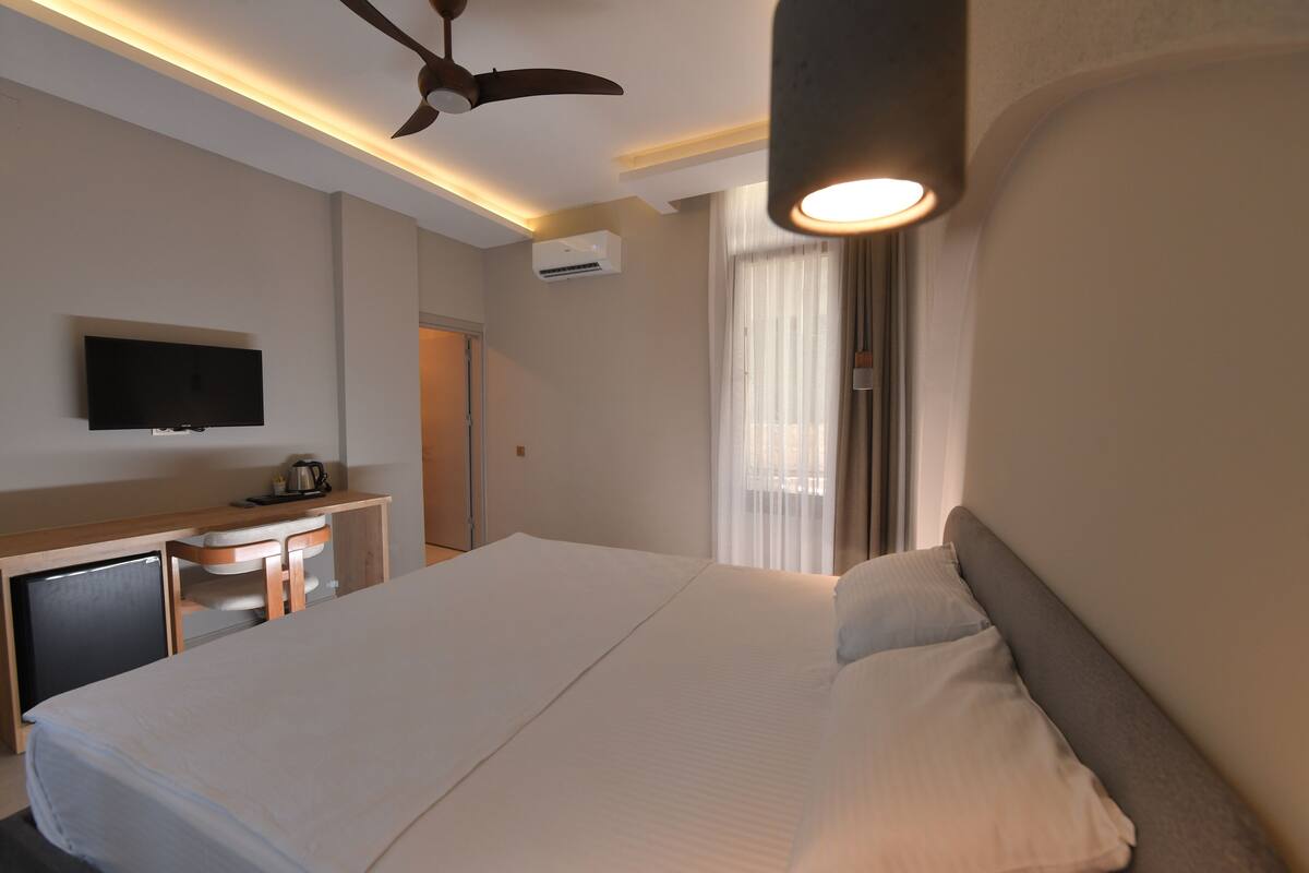 Een hotelkamer met een bed, bureau, televisie en plafondventilator.