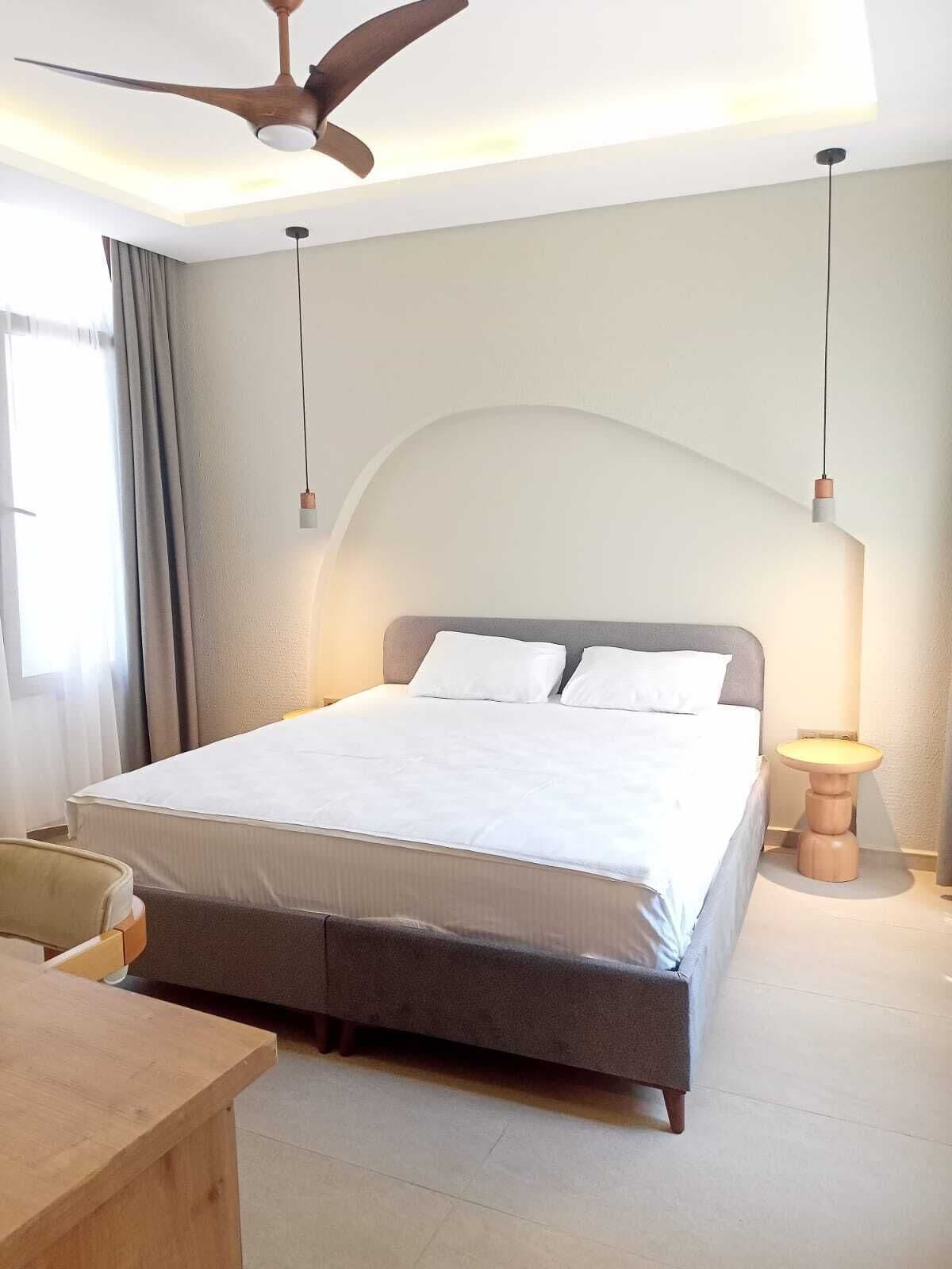A bedroom with a bed, a ceiling fan, a bedside table, and a lamp.