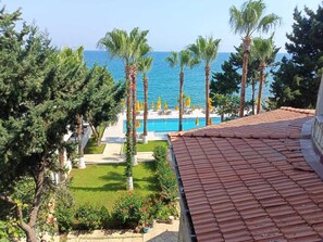 A pool area with a clear view of the sea, surrounded by palm trees and a tiled roof. - Casalita Hotel (Erdemli)