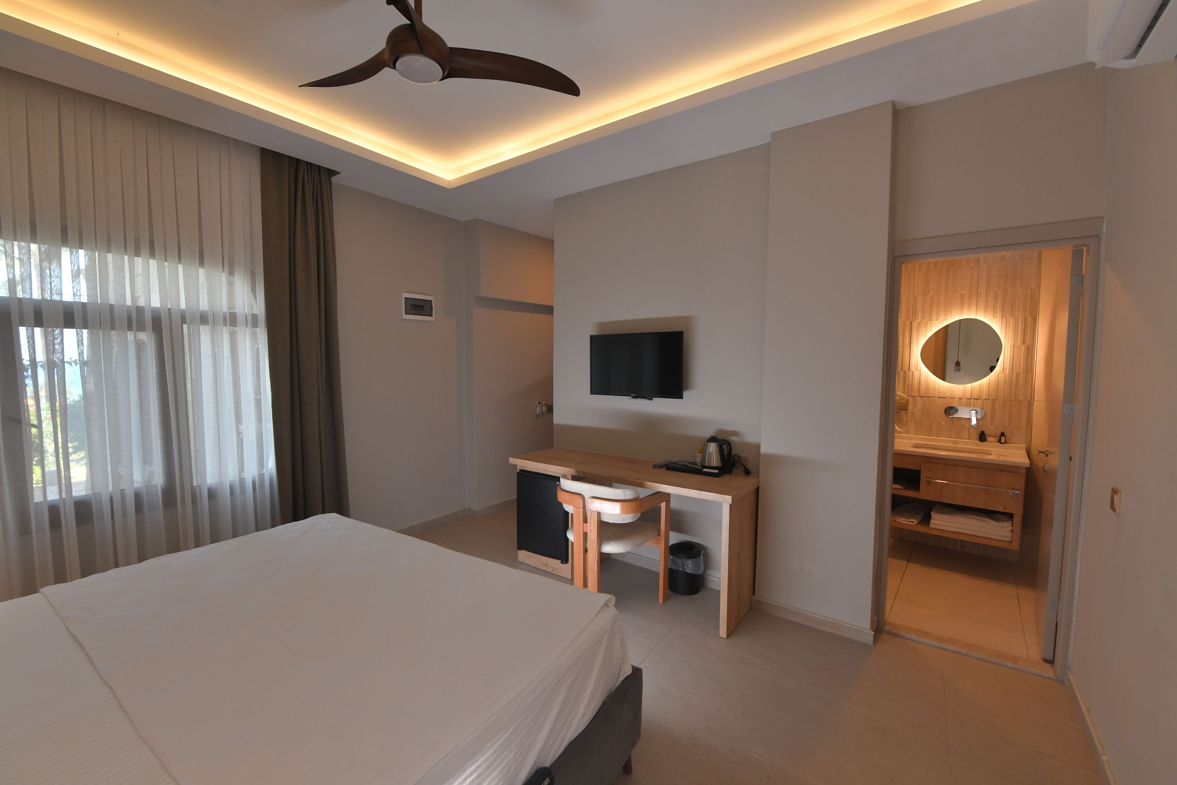 Habitación de hotel con cama, escritorio, silla, televisor y baño con espejo y lavabo.