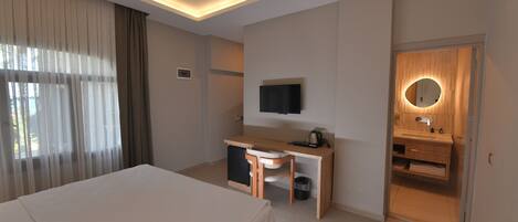 Habitación de hotel con cama, escritorio, silla, televisor y baño con espejo y lavabo.