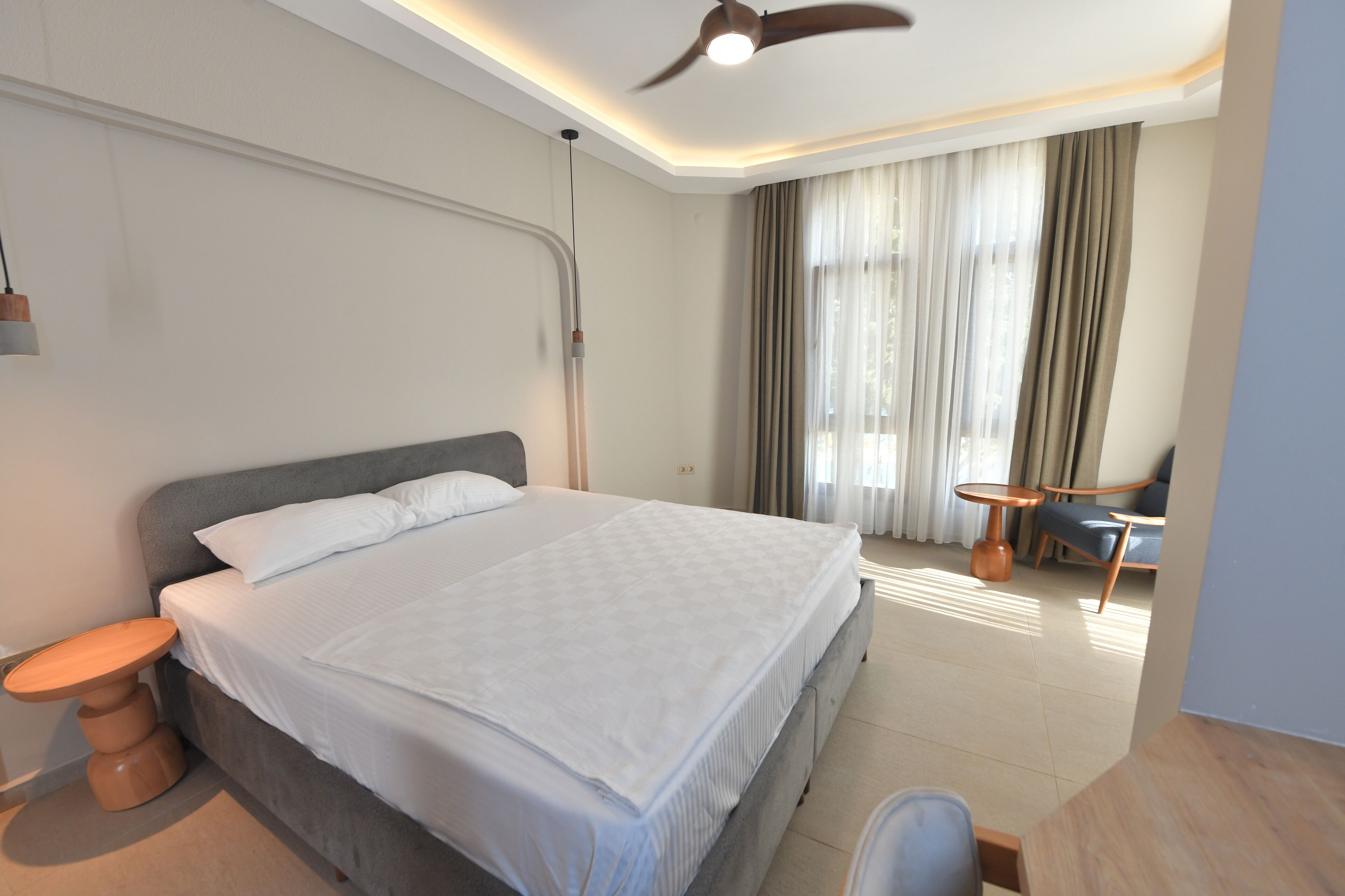 A modern hotel room with a large bed, a ceiling fan, a small table, and a chair.