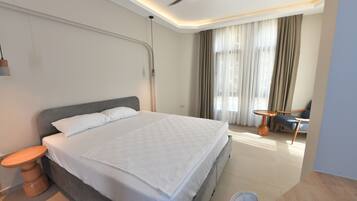 A modern hotel room with a large bed, a ceiling fan, a small table, and a chair.