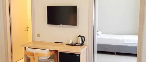 A hotel room with a wooden desk, a television mounted on the wall, a bed, and a small refrigerator.