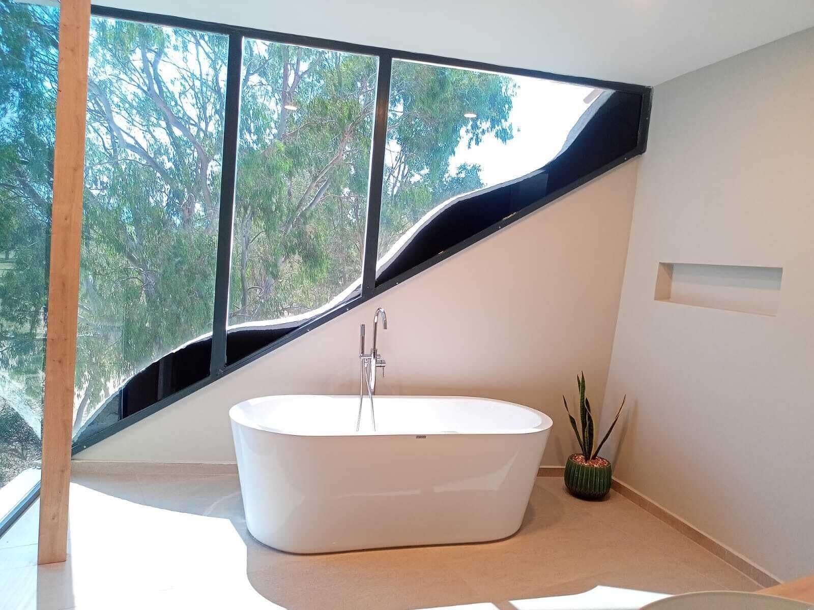Un baño moderno con una bañera independiente, ventanas amplias y vistas a árboles.