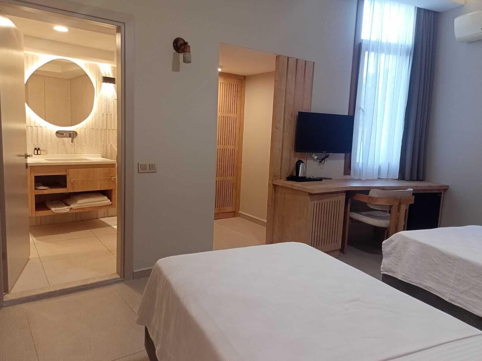 A hotel room with a bathroom, a desk, and two beds.