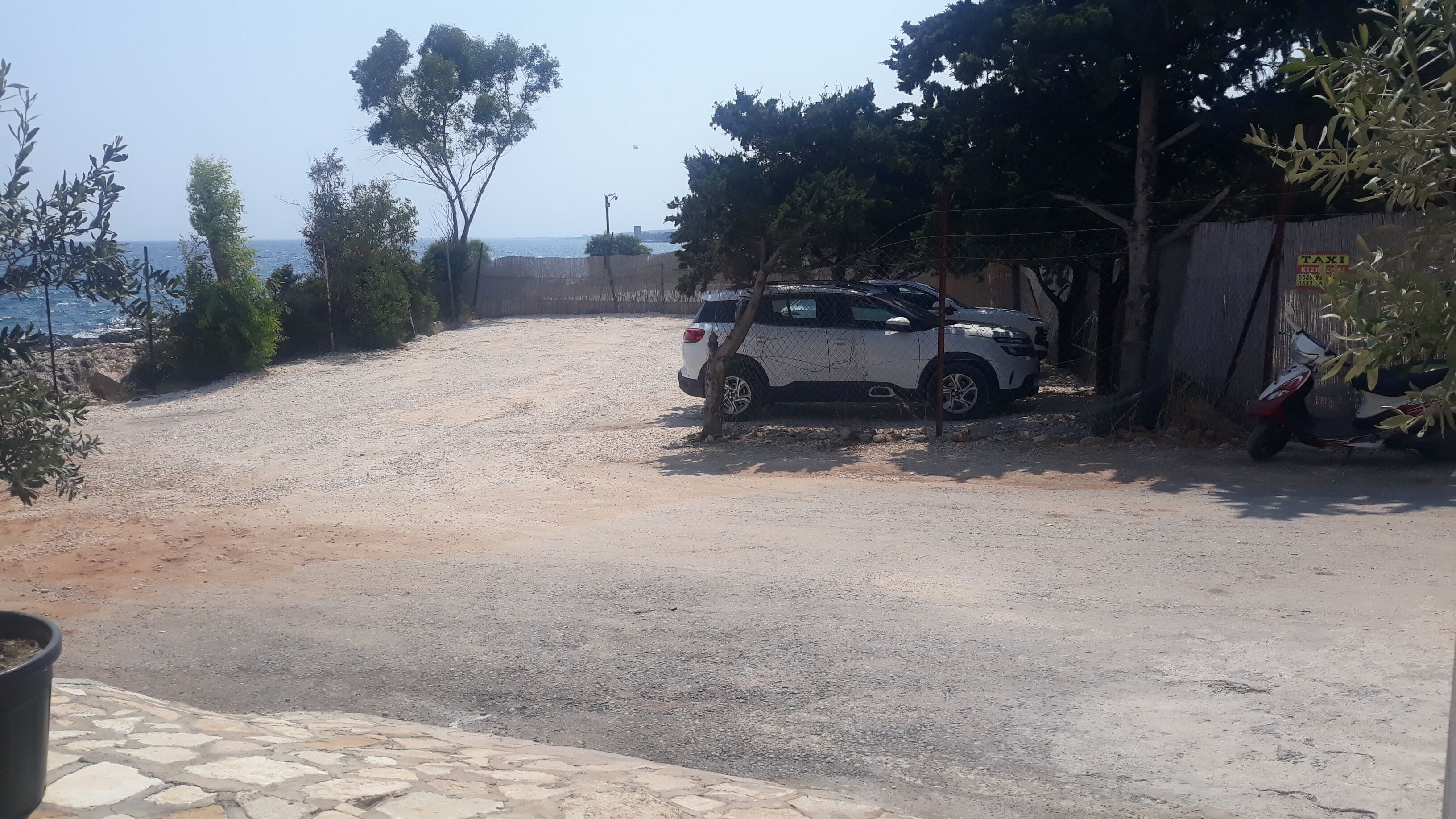 A gravel driveway leading to a white SUV parked near a fence with a sign that reads "TAXI."
