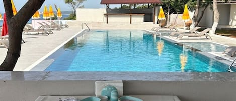Zona de comedor junto a la piscina con una mesa preparada para el desayuno, con vistas a una pileta y un edificio con tejado rojo.