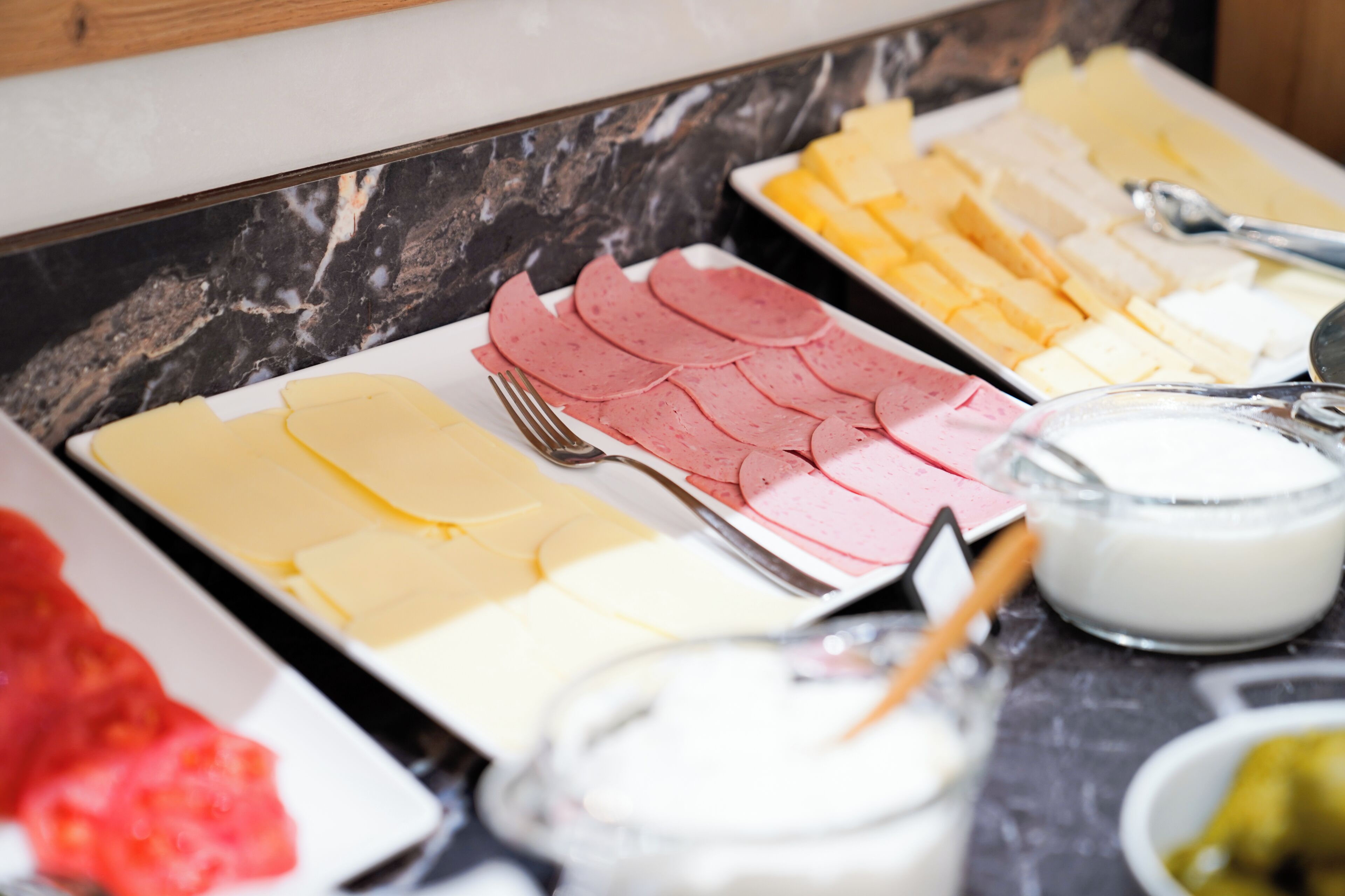 Een ontbijtbuffet met verschillende kazen, vleeswaren en melk.