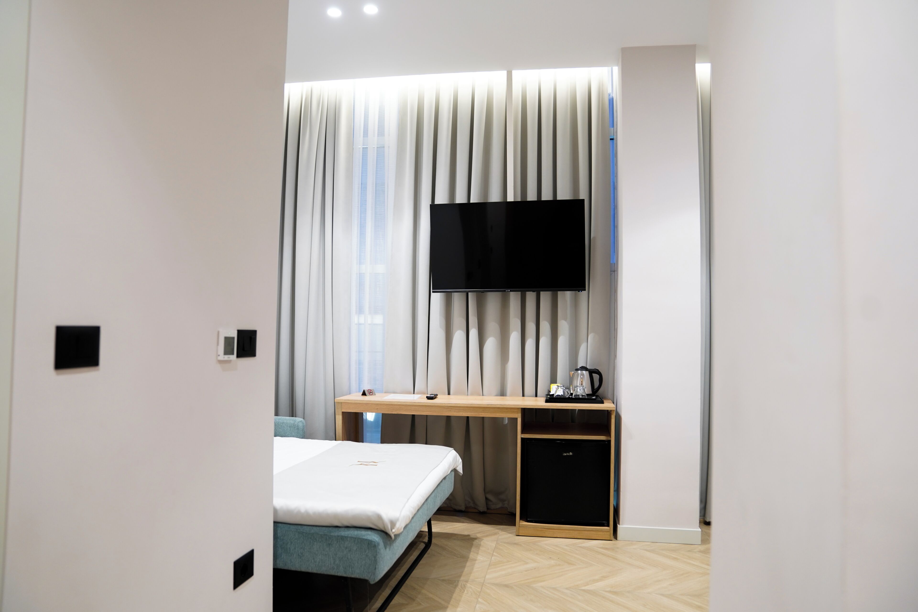 A modern hotel room with a bed, a desk, a television, and a small cabinet.