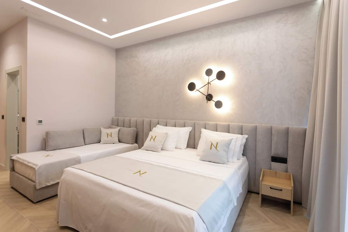 A modern hotel room with two beds, a small wooden side table, and a wall-mounted light fixture.