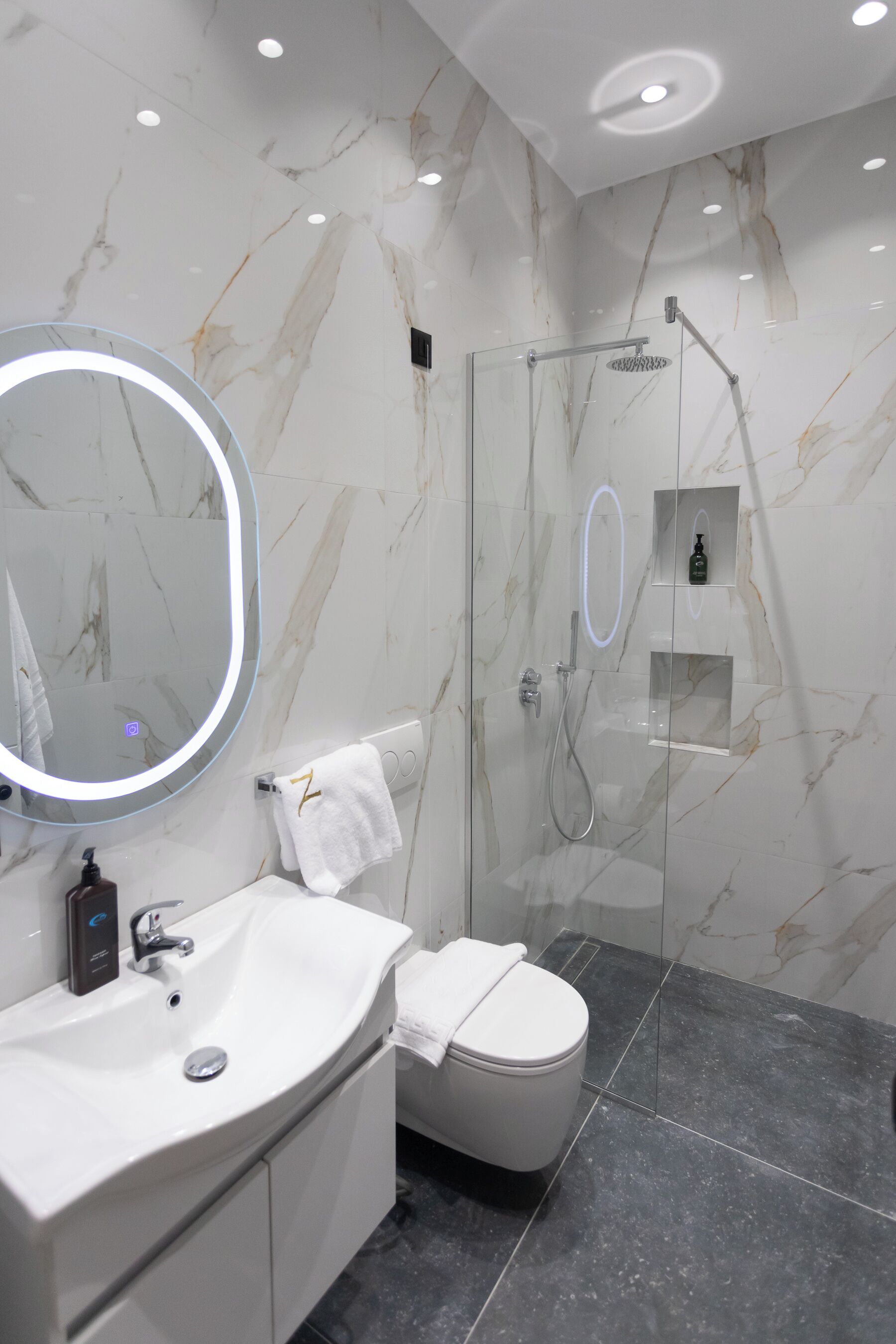 Une salle de bain moderne avec un mur en marbre, une douche à parois de verre, un lavabo blanc et des toilettes.