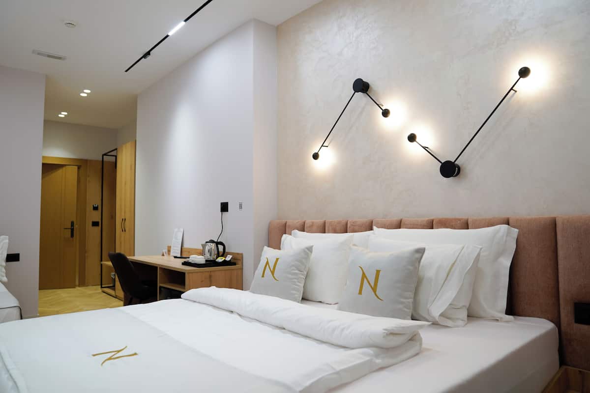 A modern hotel room with a neatly made bed, a desk, and a wall-mounted light fixture.