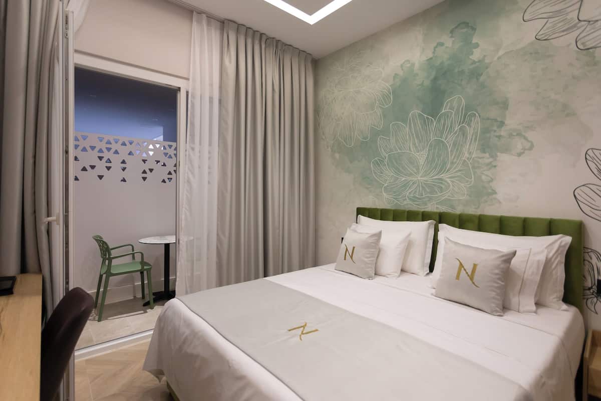 A hotel room with a bed, a green upholstered headboard, and a wall with a floral design.