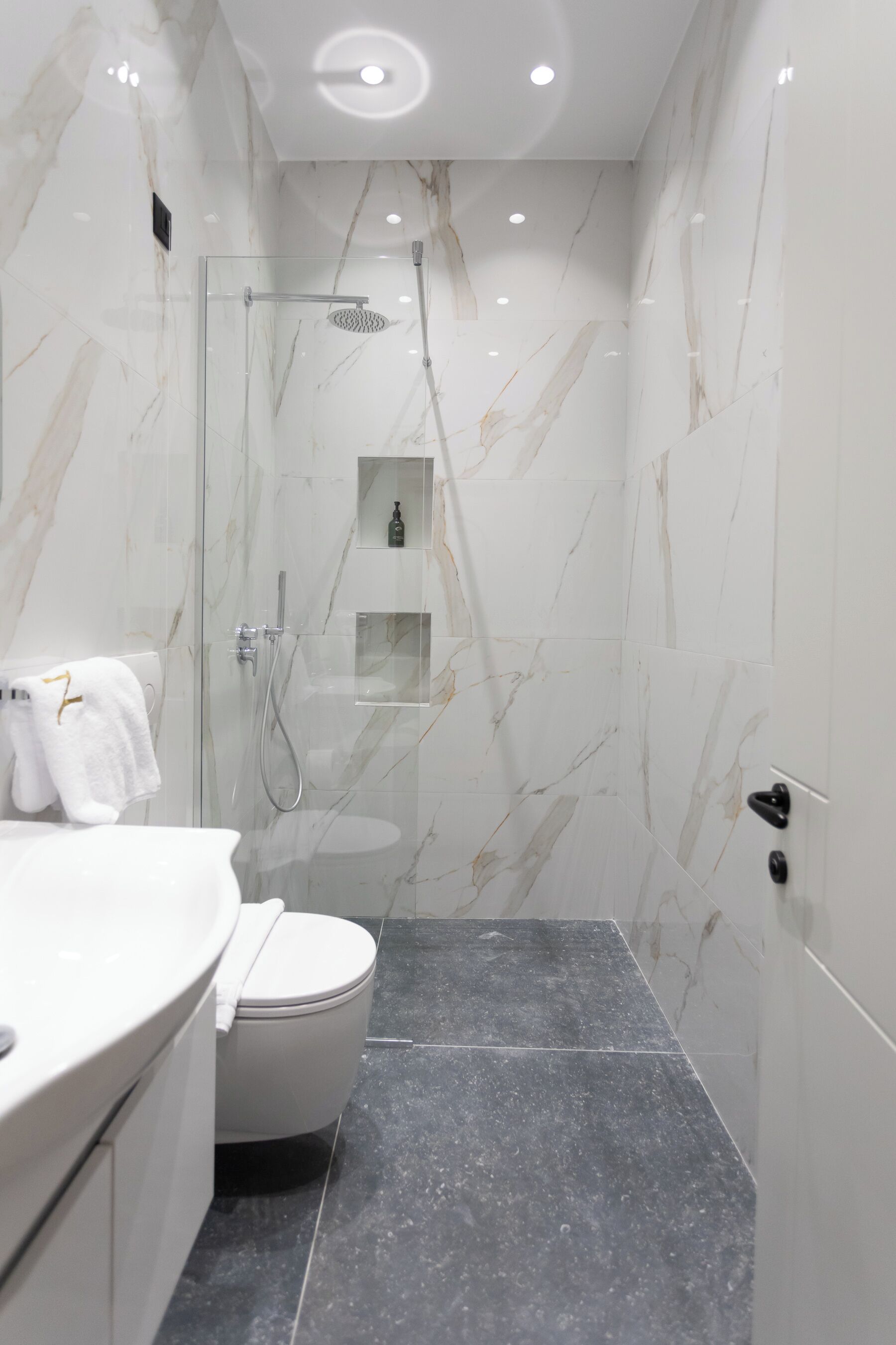 A modern bathroom with a glass-enclosed shower, a white toilet, and a marble-tiled floor.