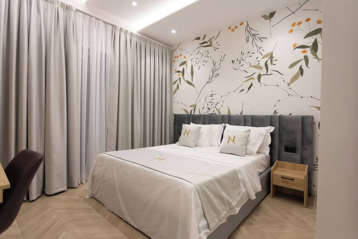 A modern hotel room with a large bed, a wooden nightstand, and a chair.