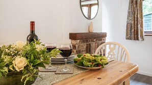 Een eettafel met een fles wijn, twee wijnglazen, een saladebord en een bloemenvaas.