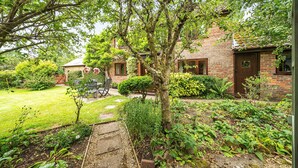 Een bakstenen huis met een verzorgde tuin, een kleine tuinhuis en een pad naar de woning.