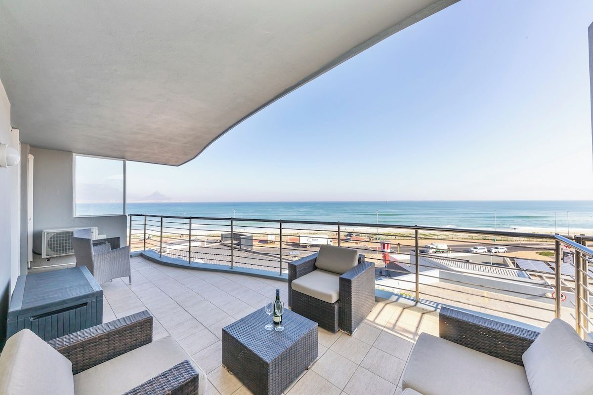 Ein Balkon mit Gartenmöbeln, Blick auf den Strand und einem klaren Himmel.