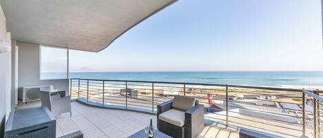 Ein Balkon mit Gartenmöbeln, Blick auf den Strand und einem klaren Himmel.