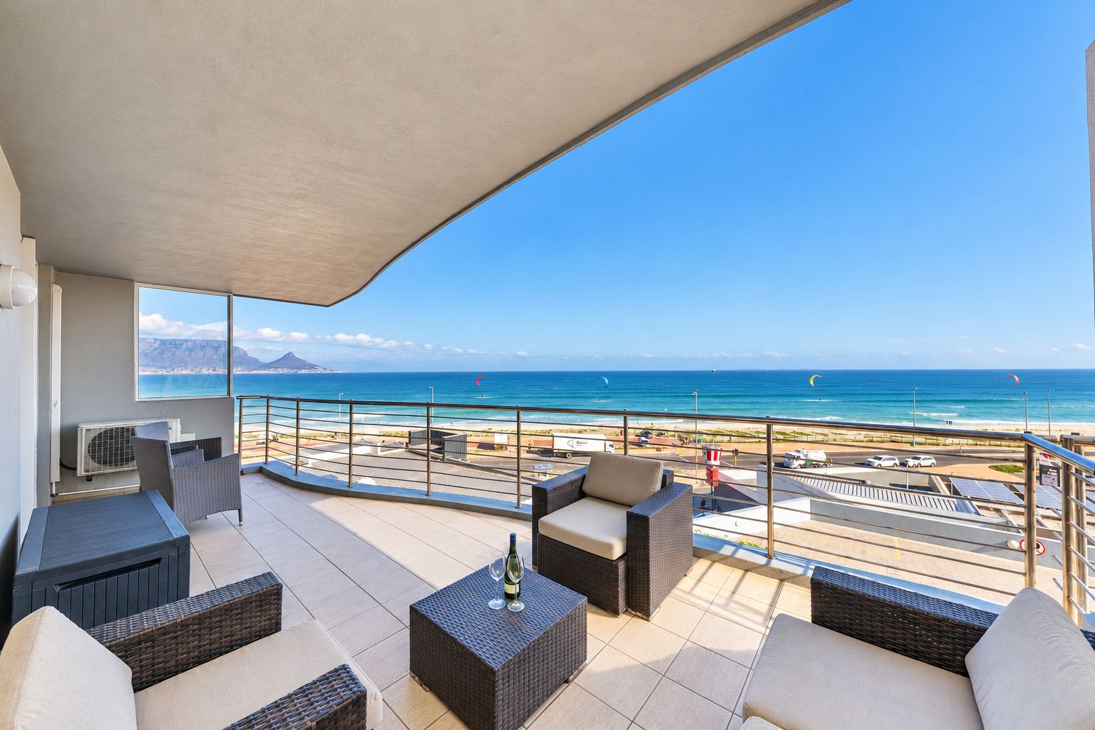 A balcony with outdoor furniture, a view of the beach, and a clear sky.