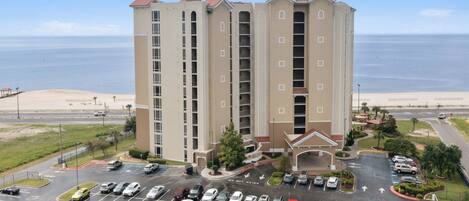 A multi-story hotel with a parking lot in front, located near a beach.