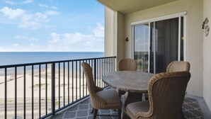 Un balcon avec des fauteuils en osier et une table, donnant sur une plage sous un ciel dégagé.