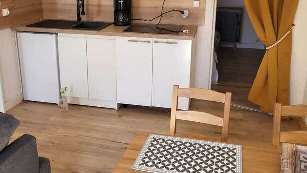 Una cucina compatta con mobili bianchi, uno schienale rosso e una macchina da caffè nera.