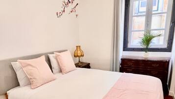 A neatly made bed with a white and pink bedspread, a wooden headboard, and a chandelier above.