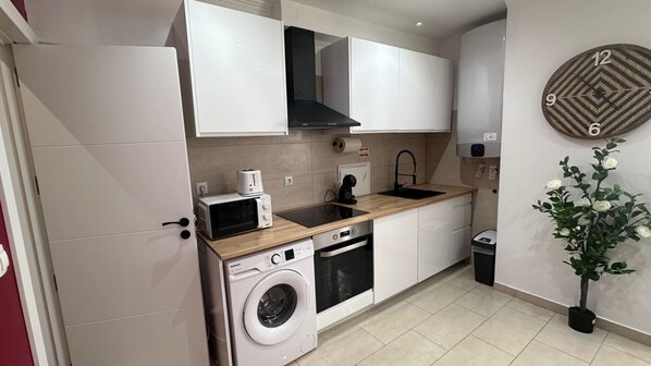 A modern kitchen with white cabinets, a microwave, a toaster, a sink, a stove, and a washing machine.