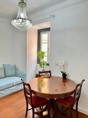 Un coin repas comprenant une table ronde en bois, quatre chaises, un lustre, une plante en pot et un canapé.