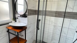 A bathroom with a glass-enclosed shower, a sink with a mirror, and a shelf with toiletries. - Sintra Historic Centre Romantism Capital (Sintra)