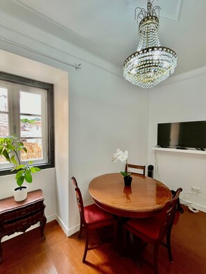 A dining area with a wooden table, red chairs, a chandelier, a potted plant, and a TV on the wall.