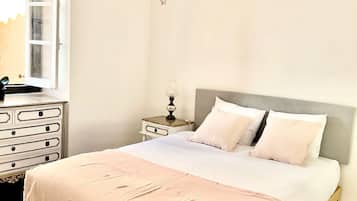 Een slaapkamer met een groot bed, een nachtkastje, een dressoir, een raam en een kroonluchter.