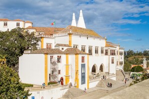 A historic building with a prominent staircase leading to the entrance, a flag, and a clear sky.