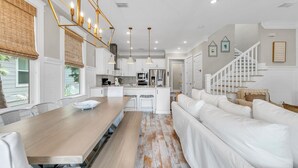 Un salón amplio con una mesa de comedor de madera, sofás blancos y una escalera que conduce a un nivel superior.