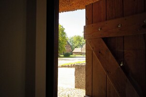Una puerta de madera con base de piedra, que da a un espacio exterior con un camino adoquinado y edificios tradicionales.