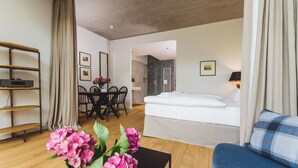 A hotel room with a bed, a seating area with a table and chairs, a TV on a shelf, and a bathroom visible through an open door. - Gut Damp (Damp)