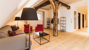 A loft-style living room with exposed wooden beams, a sofa, a red armchair, a coffee table, and a lamp. - Gut Damp (Damp)